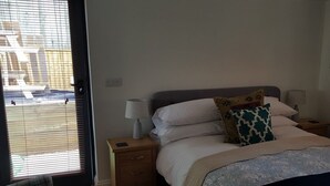 Une chambre à coucher avec un lit, des tables de chevet, une lampe et une vue sur l’extérieur, visible à travers une porte.