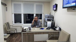 A man sitting at a desk in an office with a computer, printer, and a TV mounted on the wall. - Beyazithan (Istanbul)