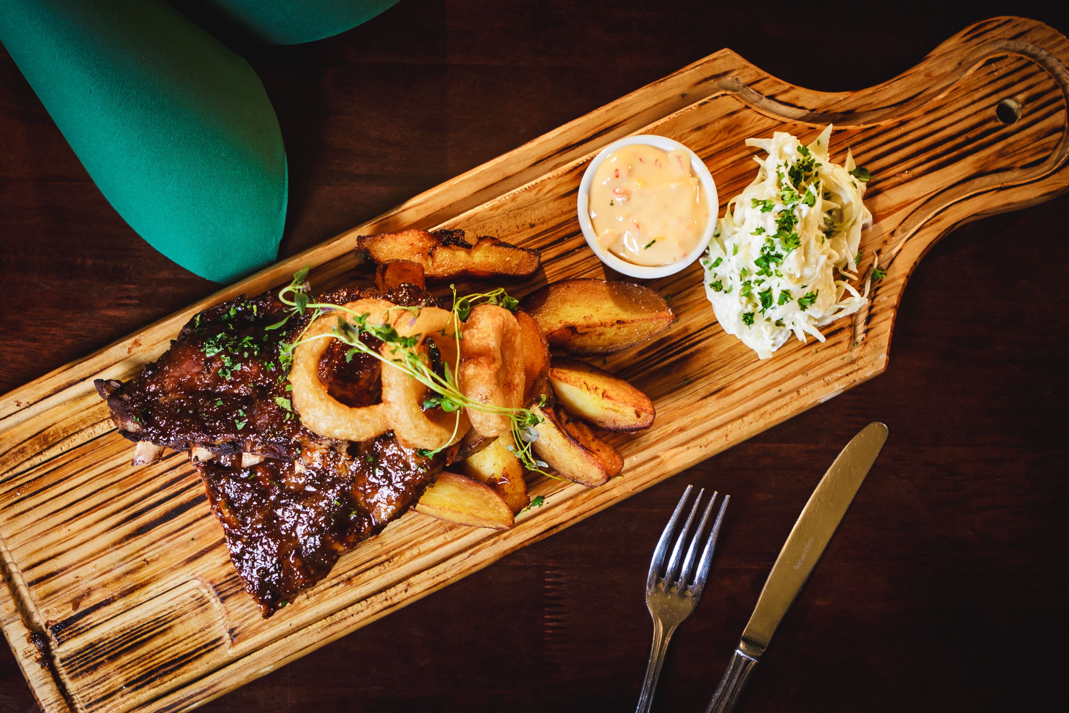 A wooden serving board with grilled meat, roasted potatoes, and a side of sauerkraut and sauce.