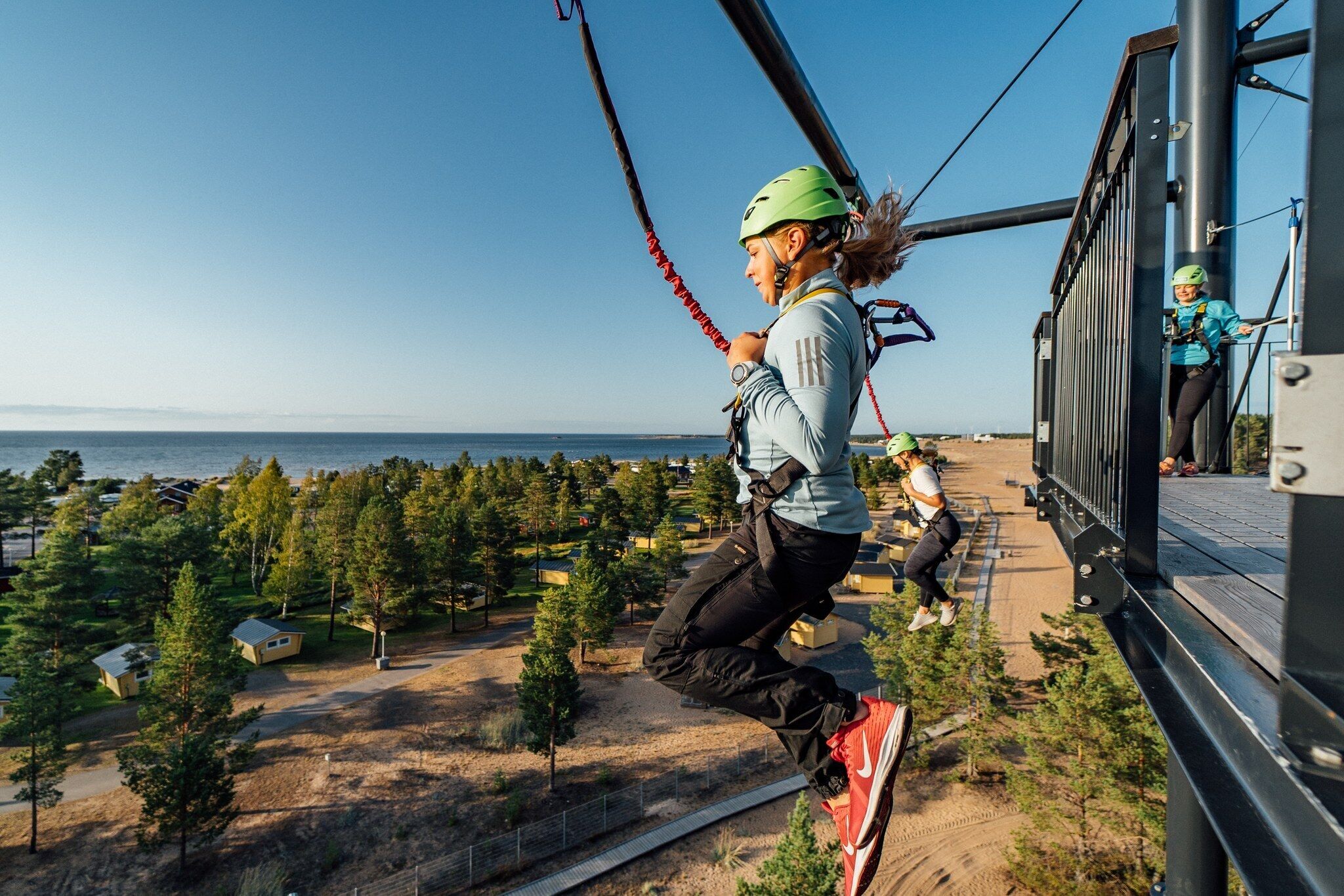 Henkilö laskeutuu köyden varassa alas, ja taustalla avautuu kaunis näkymä metsään ja vesistöön.