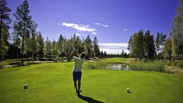 Iemand op een golfbaan met een heldere lucht, bomen en een vijver.