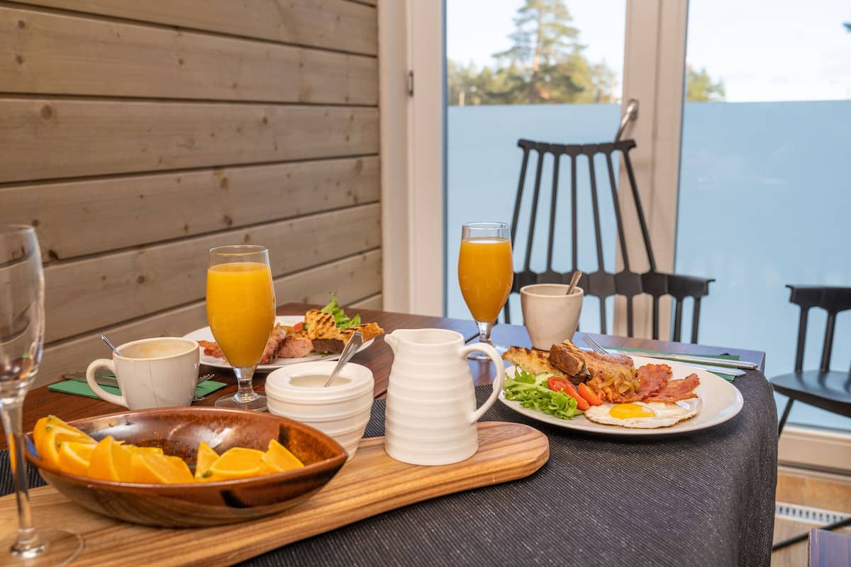 Mesa de café da manhã com fatias de laranja, um jarro e pratos com ovos, bacon e torradas.