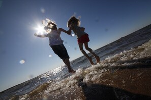 Two children jumping into the ocean at sunset.