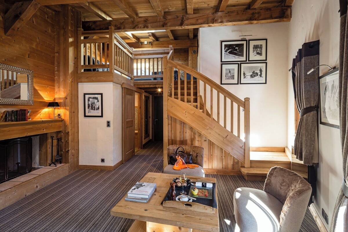 A cozy wooden interior with a staircase, a dining area with a table set for two, and a fireplace.