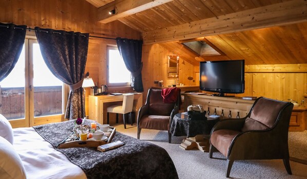 A cozy log cabin room with a bed, a desk, a TV, and a dining area. - Hôtel Le Fer à Cheval (Megeve)