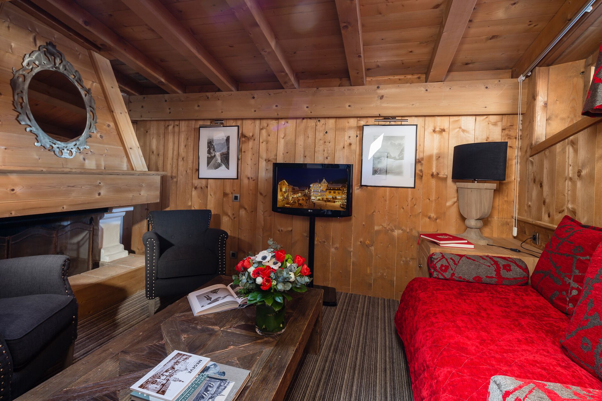 A cozy room with wooden walls, a fireplace, a television, a sofa, and a coffee table with books and flowers.
