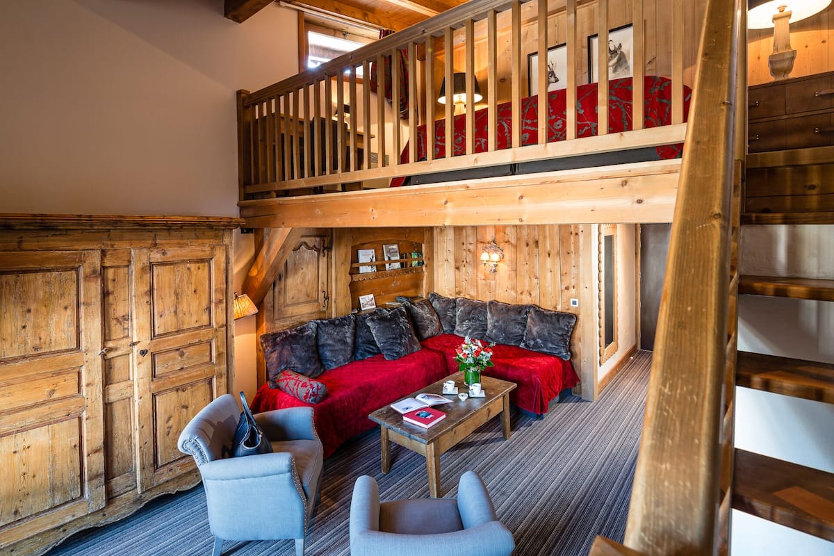 A cozy room with a red sofa, two armchairs, a wooden coffee table, and a wooden staircase.