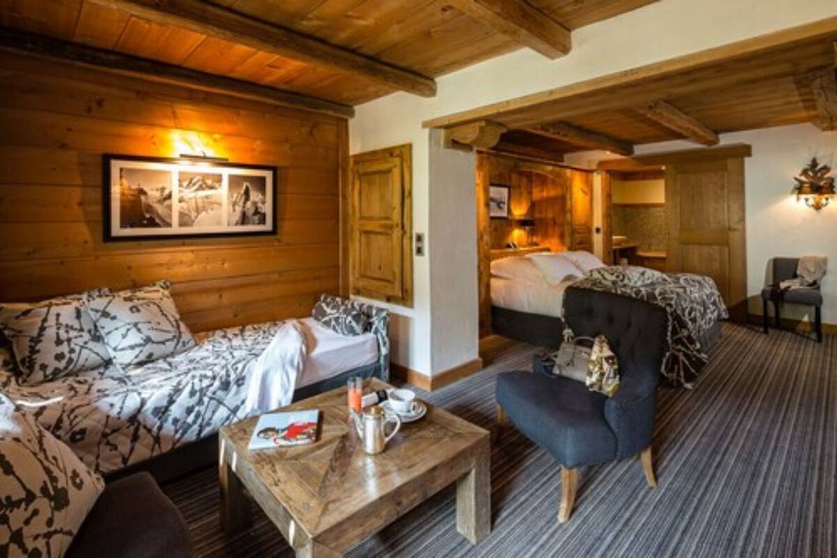 A cozy room with a bed, a sofa, a coffee table, and a chair. There is a framed picture on the wall and a wooden ceiling.