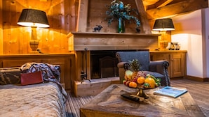 Una habitación acogedora con chimenea, paredes de madera, un sillón cómodo, una cama y un frutero sobre una mesa de madera.