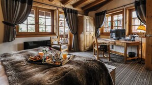 Una habitación acogedora con techo de madera, una cama con manta de piel, una bandeja de desayuno, un escritorio con computadora y una ventana con cortinas.