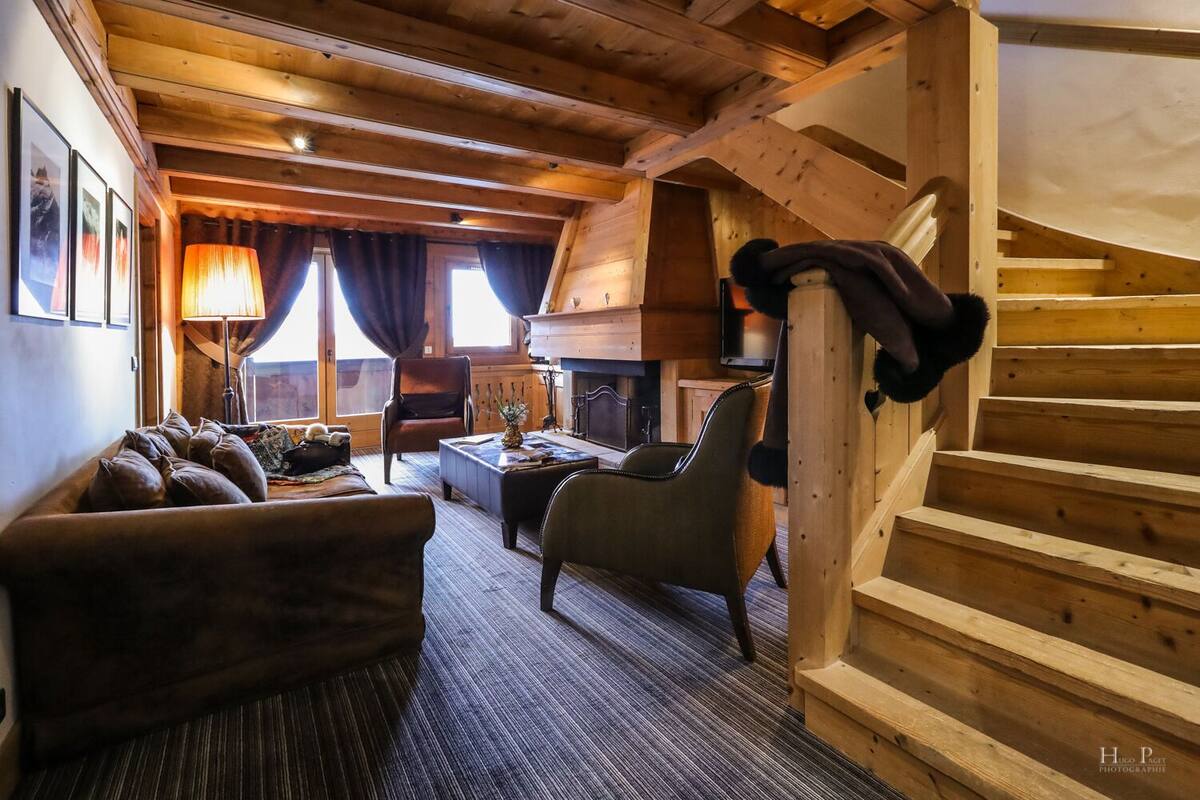 A cozy log cabin interior with a fireplace, wooden staircase, and comfortable seating.