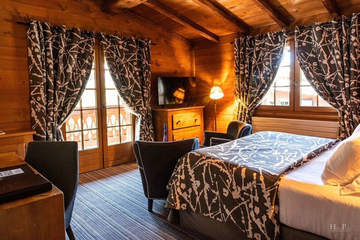 A cozy wooden cabin room with a bed, two chairs, a desk, and a lamp.