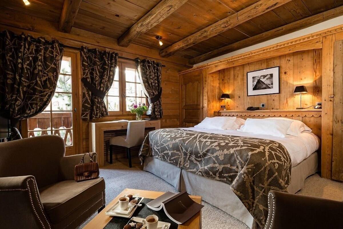 A cozy room with a bed, desk, and chair, wooden walls, and a fireplace.