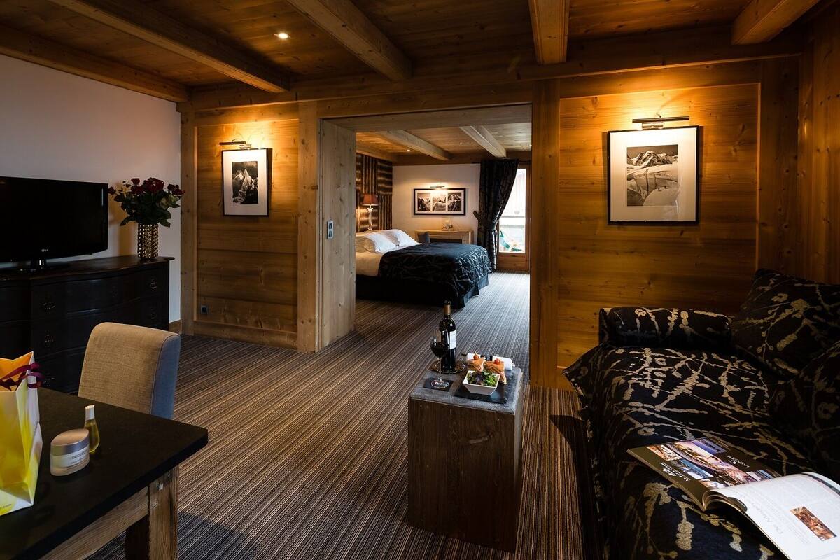 A cozy room with a bed, a TV, a dining area with a table and chairs, and a small coffee table with a bottle and a glass.