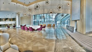 A spacious lobby with a modern design, featuring a central seating area with purple chairs, a polished marble floor, and large, star-shaped hanging lights. - The Ankara Hotel (Ankara)