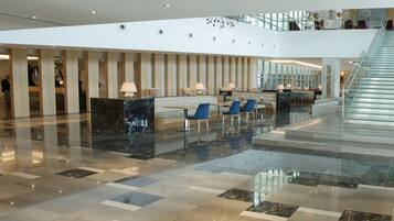 A spacious lobby with a marble floor, seating area, and a staircase leading to an upper level.