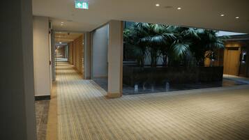 A hotel corridor with a patterned carpet, a glass wall with a view of palm trees, and a sign indicating an exit.