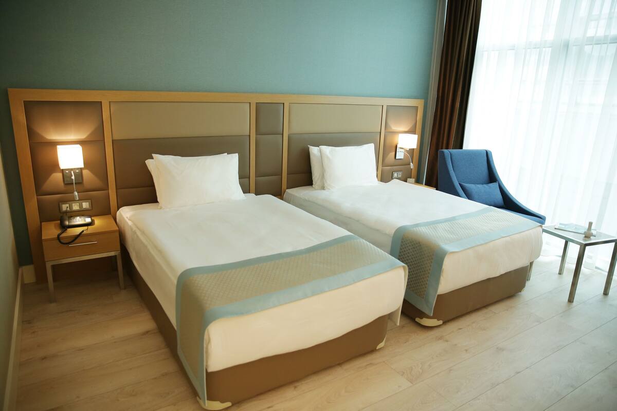 A hotel room with two beds, a nightstand with a lamp, a chair, and a small table.