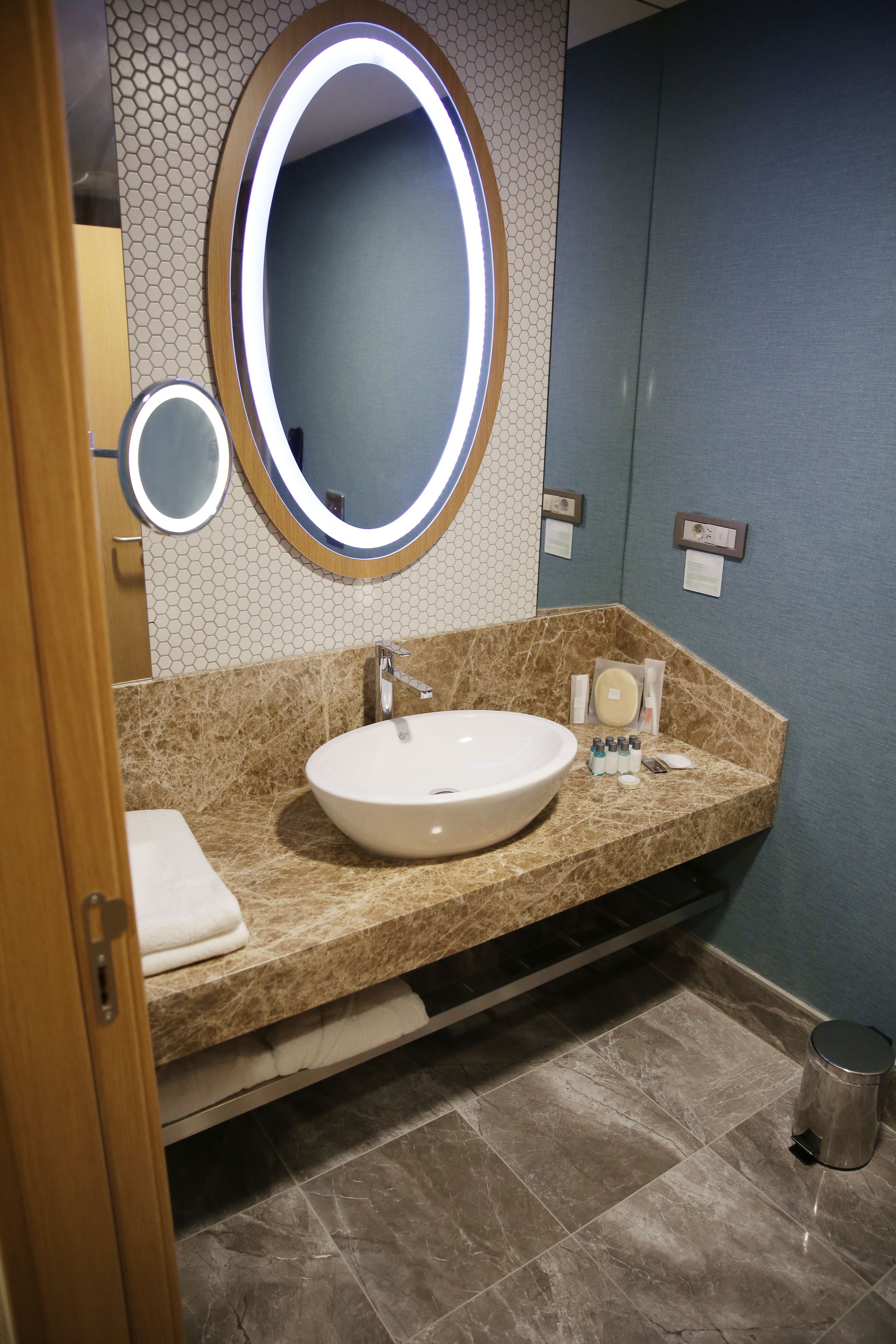 A bathroom with a large oval mirror, a sink, and a toilet.