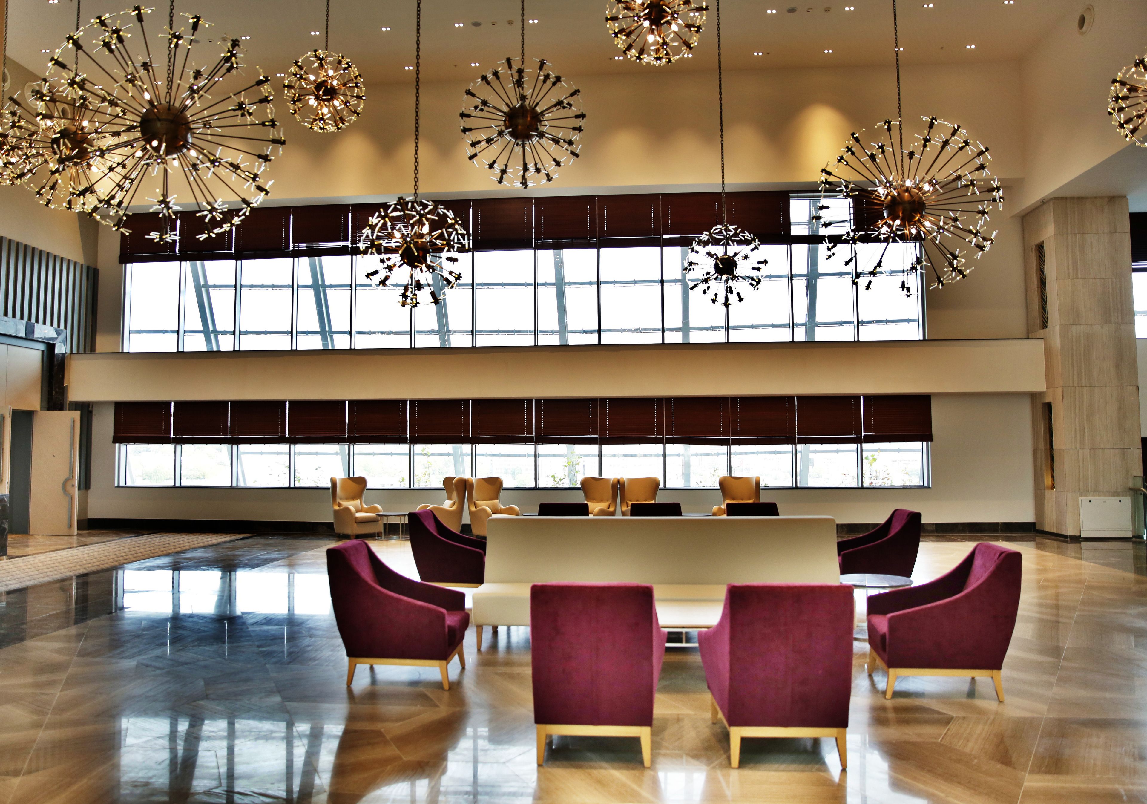 A spacious lobby with a modern chandelier, a long reception desk, and large windows allowing natural light.