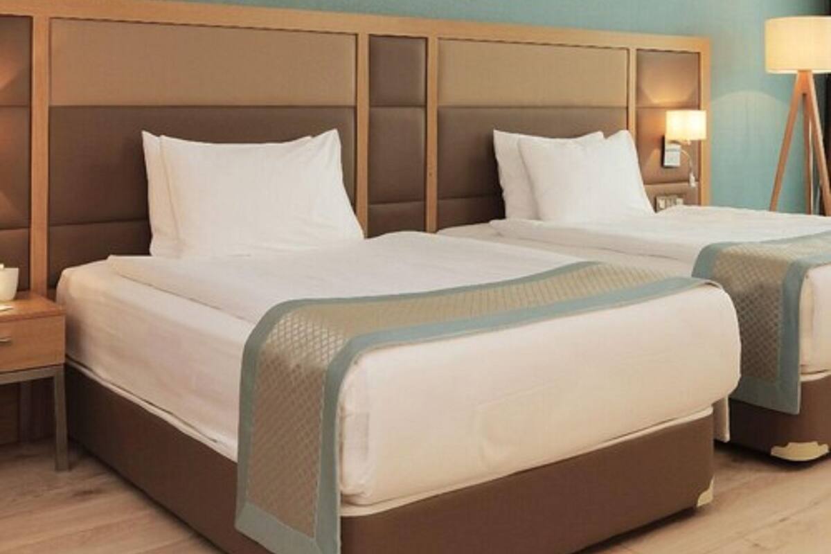 A hotel room with two beds, wooden headboards, white bedding, and a bedside lamp.