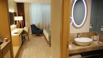 Habitació d'hotel amb llit, escriptori, cadira, un gran mirall i bany amb rentapel i productes de tocador.