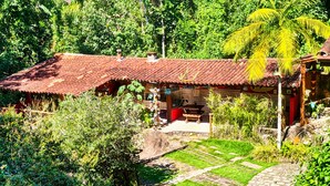 Une maison de campagne au toit de tuiles, entourée d’une végétation luxuriante et bordée d’un chemin en pierre.