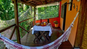 Une terrasse en bois avec un hamac, une table où sont disposés des aliments pour le petit-déjeuner et une vue sur la verdure.