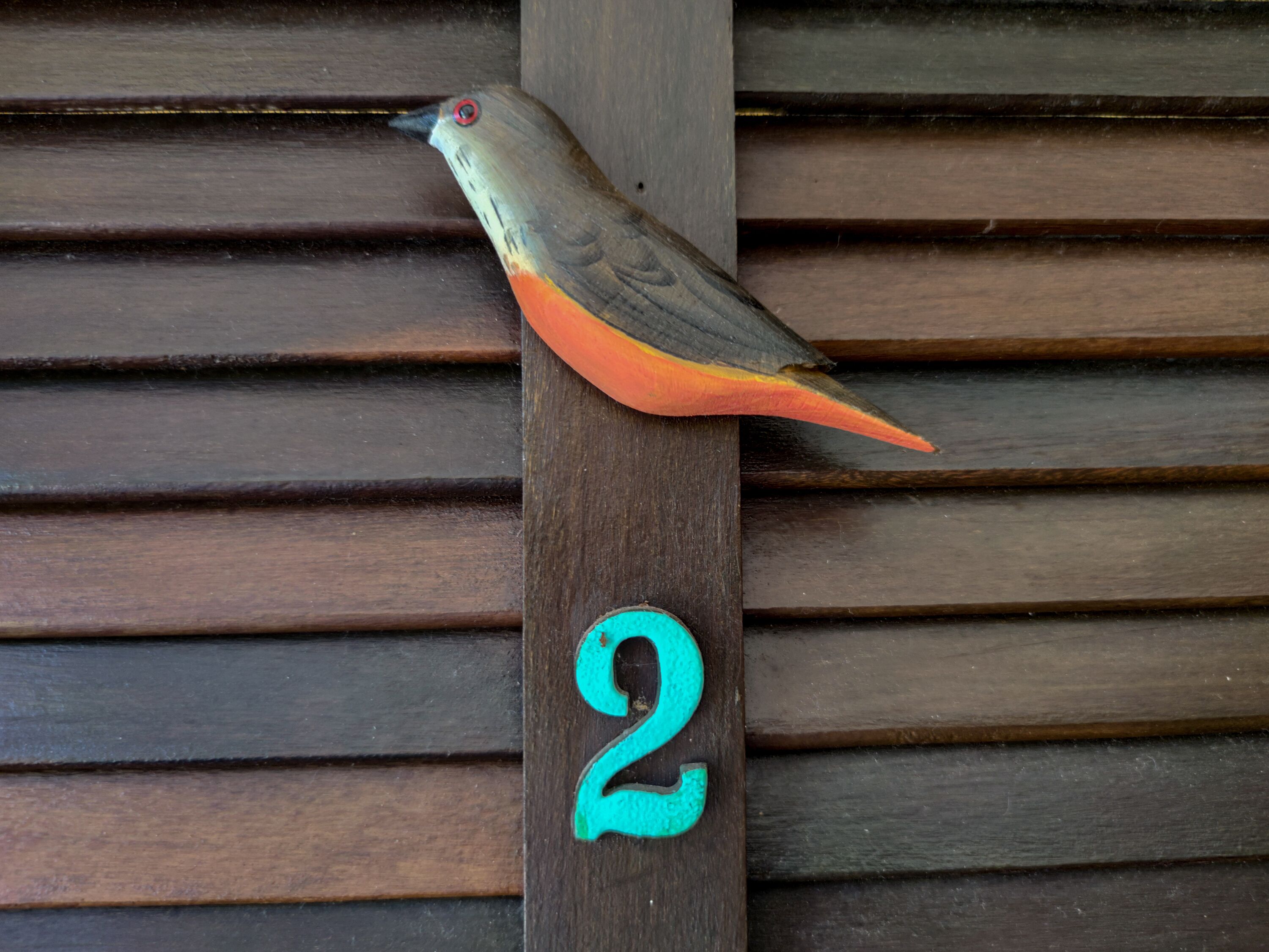 Un pájaro posado en un poste de madera con el número 2 turquesa debajo.