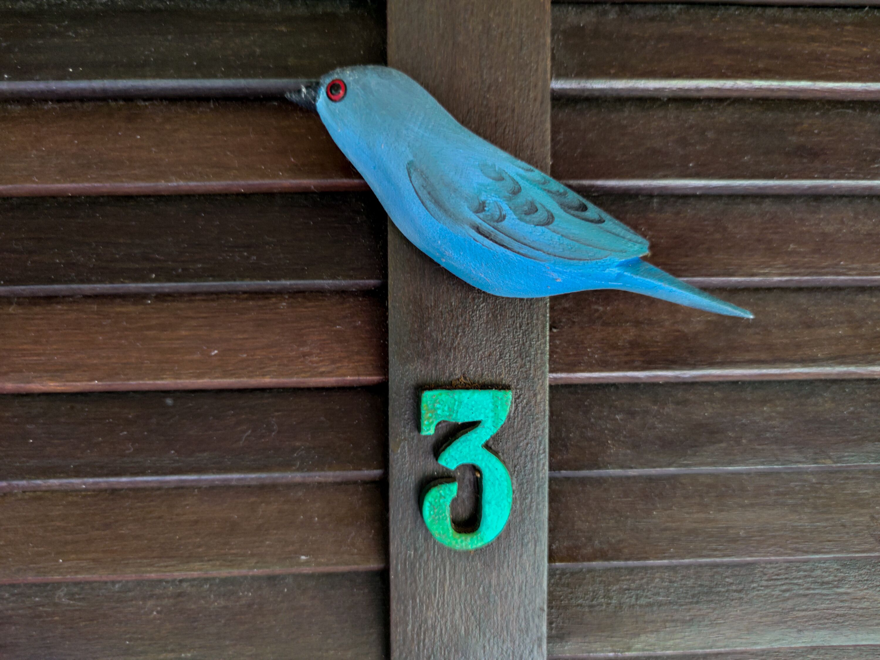 A bird-shaped mailbox on a wooden post with the number 3.