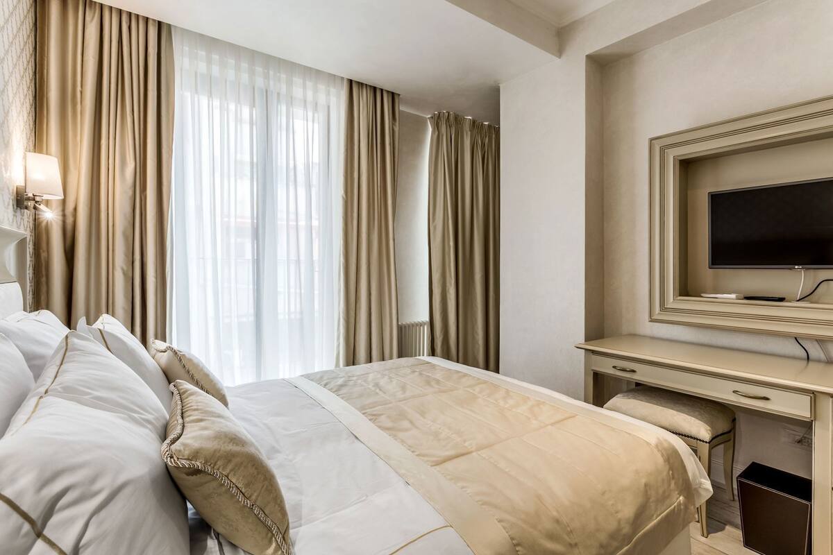A hotel room with a bed, a desk, a TV, and a window with curtains.