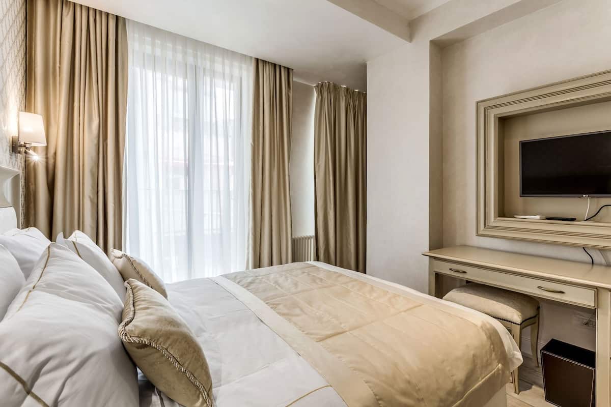 A hotel room with a bed, a desk, a TV, and a window with curtains.