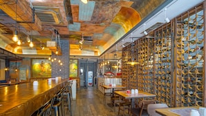 Un interior de restaurante con una larga barra de madera, varias zonas de estar y una pared de bodegas.