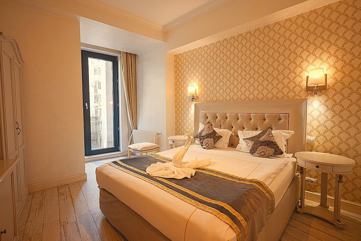 Habitación de hotel con una cama grande, un área de descanso, vistas a través de una ventana y un baño con espejo y lavamanos.