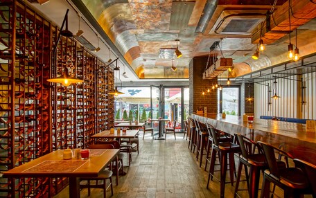 A restaurant interior with wooden tables and chairs, a bar area, and a view of the street through large windows.