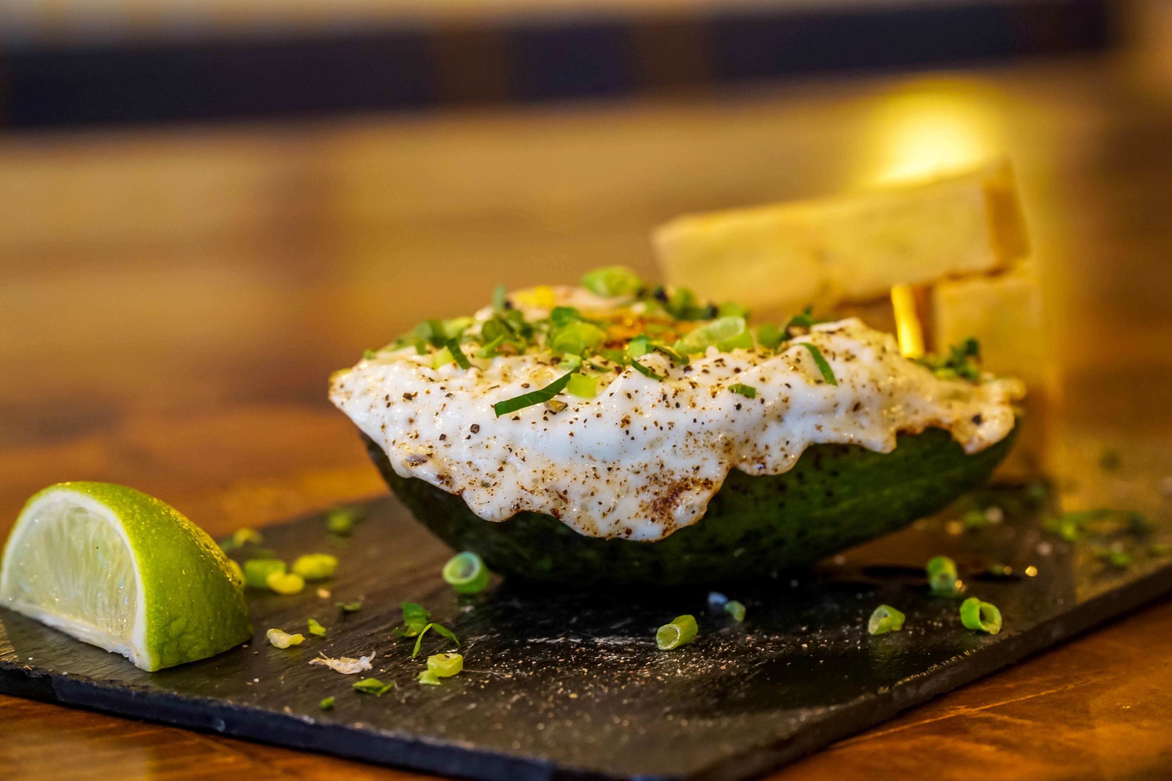 A dish with a lime wedge and chopped green onions on a dark slate board.