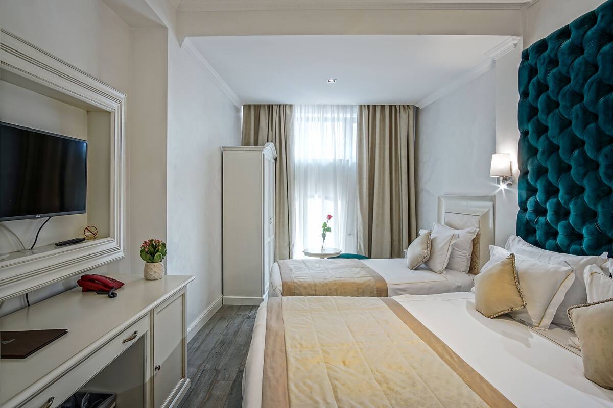A hotel room with a bed, a desk with a TV, a dresser, and a window with curtains.