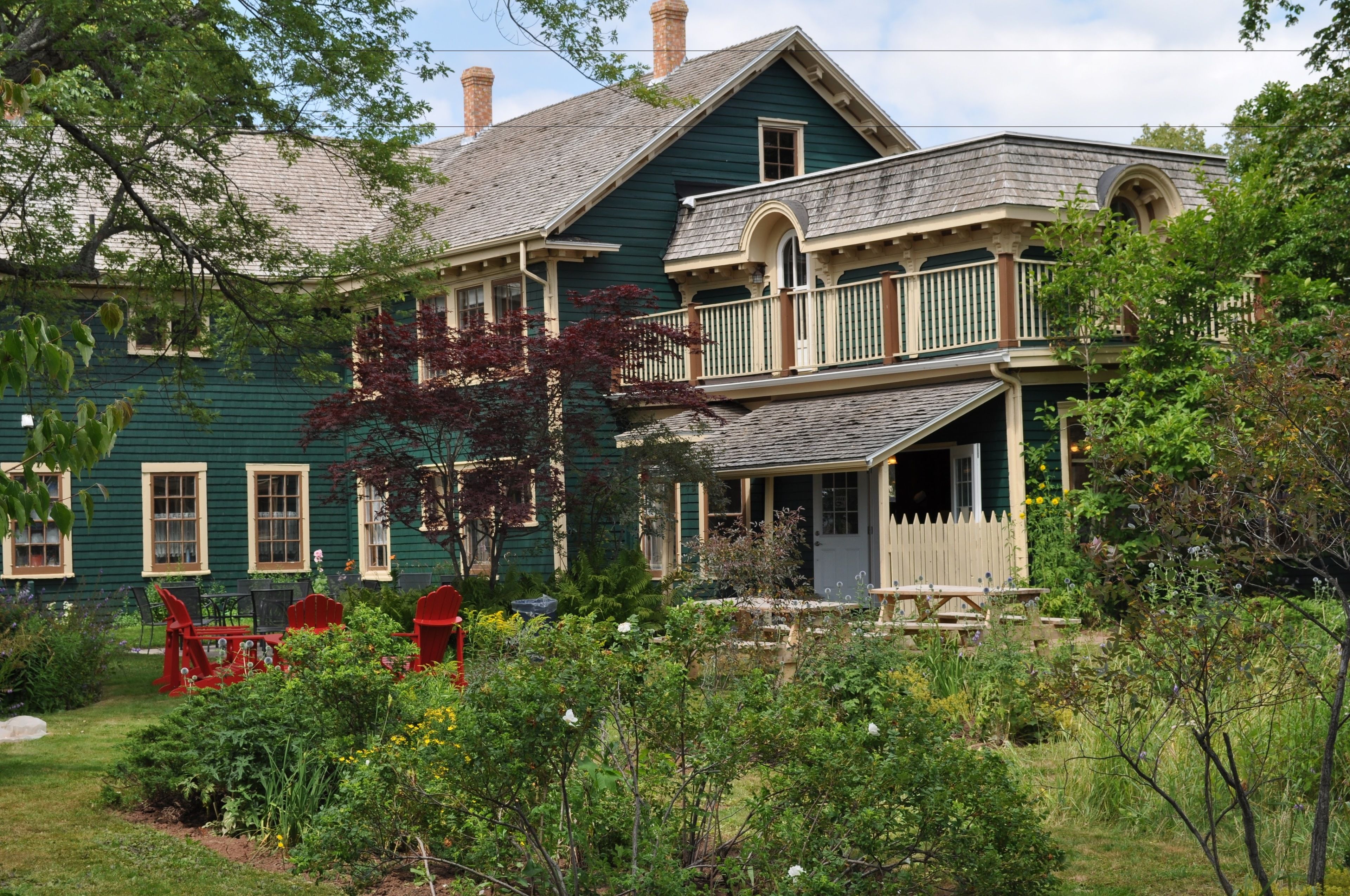 A two-story house with a porch, surrounded by a garden with various plants and flowers.