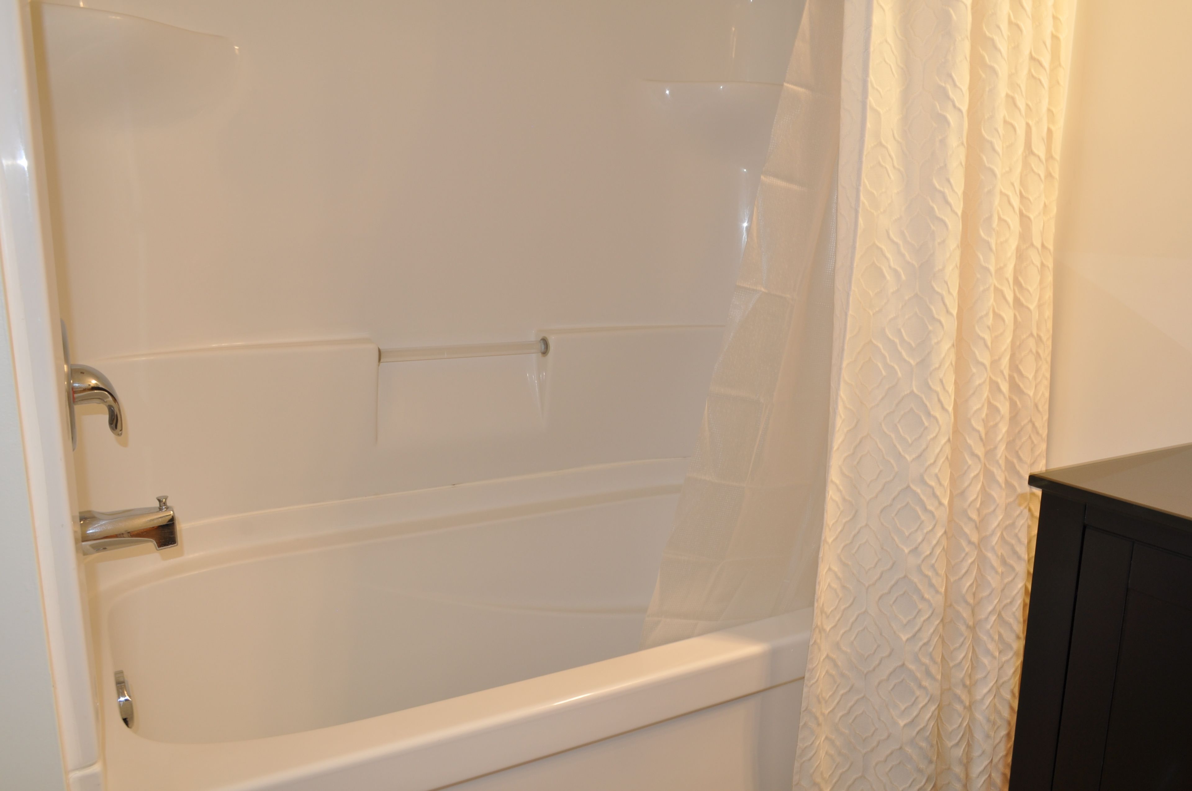 Un baño con bañera, cortina de ducha y un mueble de color oscuro.