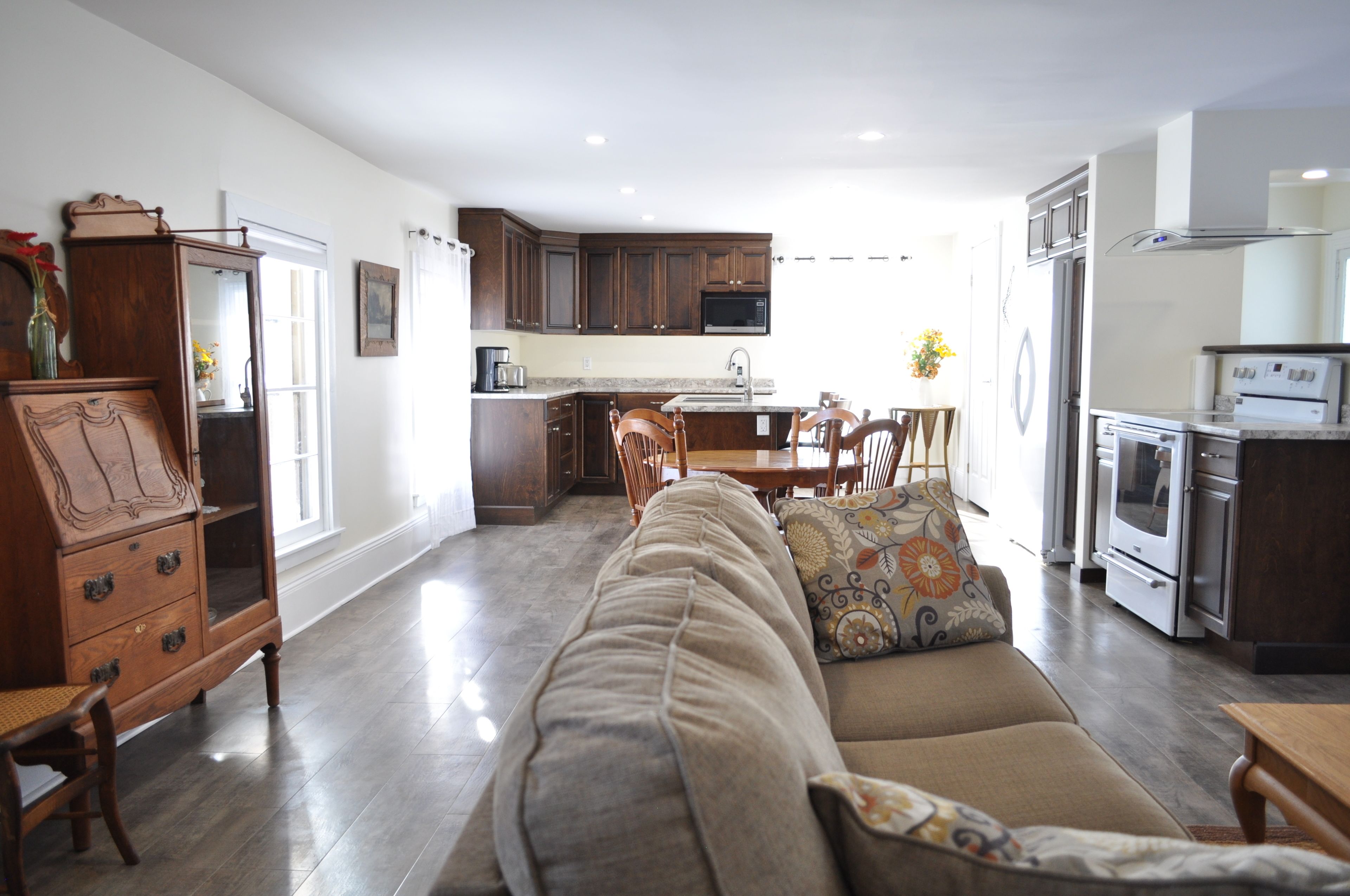 Amplia sala de estar con un sofá grande, un mueble de madera y un comedor con sillas y una mesa. Se ve una cocina con electrodomésticos modernos al fondo.