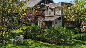 A two-story house with a balcony, surrounded by lush greenery and a well-maintained garden. - Holman's Heritage Suites (Summerside)
