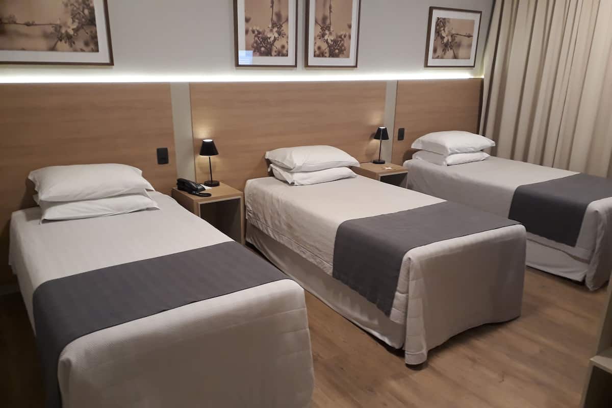A hotel room with two single beds, a wooden headboard, bedside lamps, and framed floral artwork on the wall.