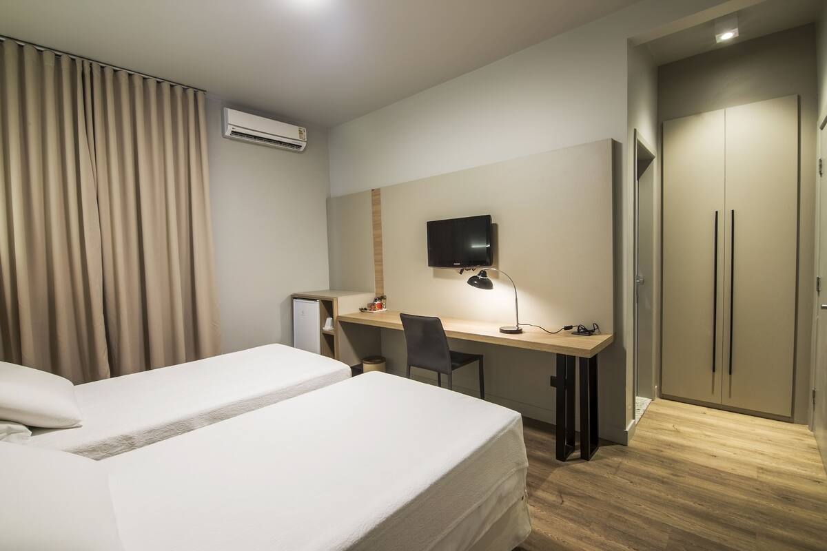 A hotel room with two beds, a desk with a chair, a television, and a wardrobe.