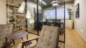 Un espacio de oficina moderno con una pared divisoria de vidrio, mobiliario de madera y una planta grande en maceta.