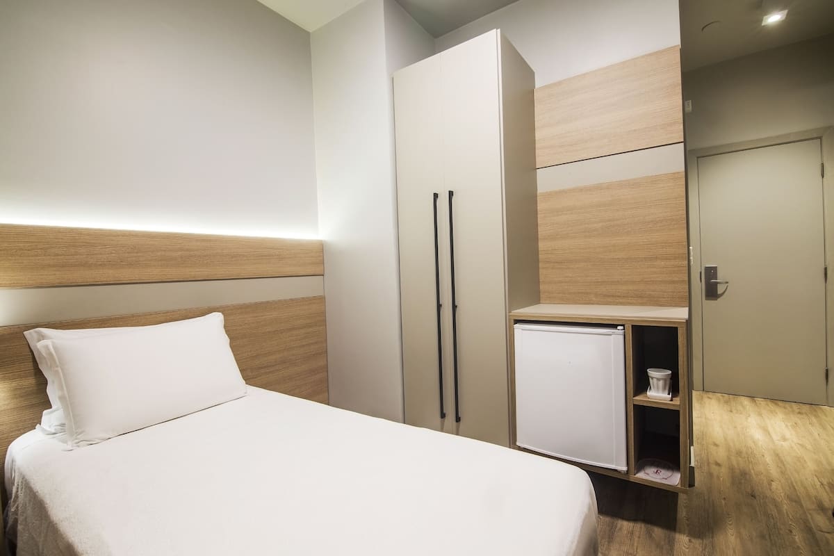 A hotel room with a bed, a wardrobe, and a small refrigerator.
