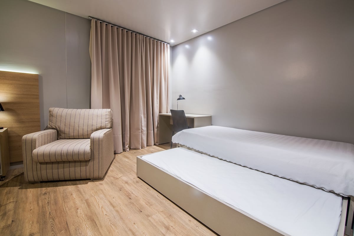 A modern hotel room with a large bed, a seating area with a chair, a desk, and a lamp.