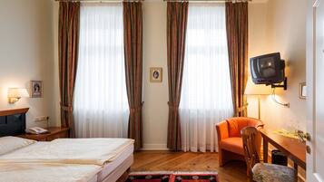 A hotel room with a bed, a desk with a chair, a television, and curtains.