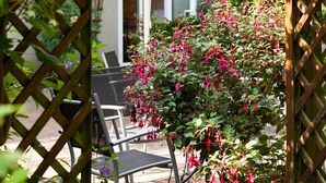 A garden area with a wooden pergola, a potted plant with pink flowers, and a white umbrella. - Hotel Schlossgarten (Neustrelitz)