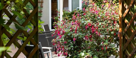Un jardín con una pérgola de madera, una planta en maceta con flores rosas y un paraguas blanco.