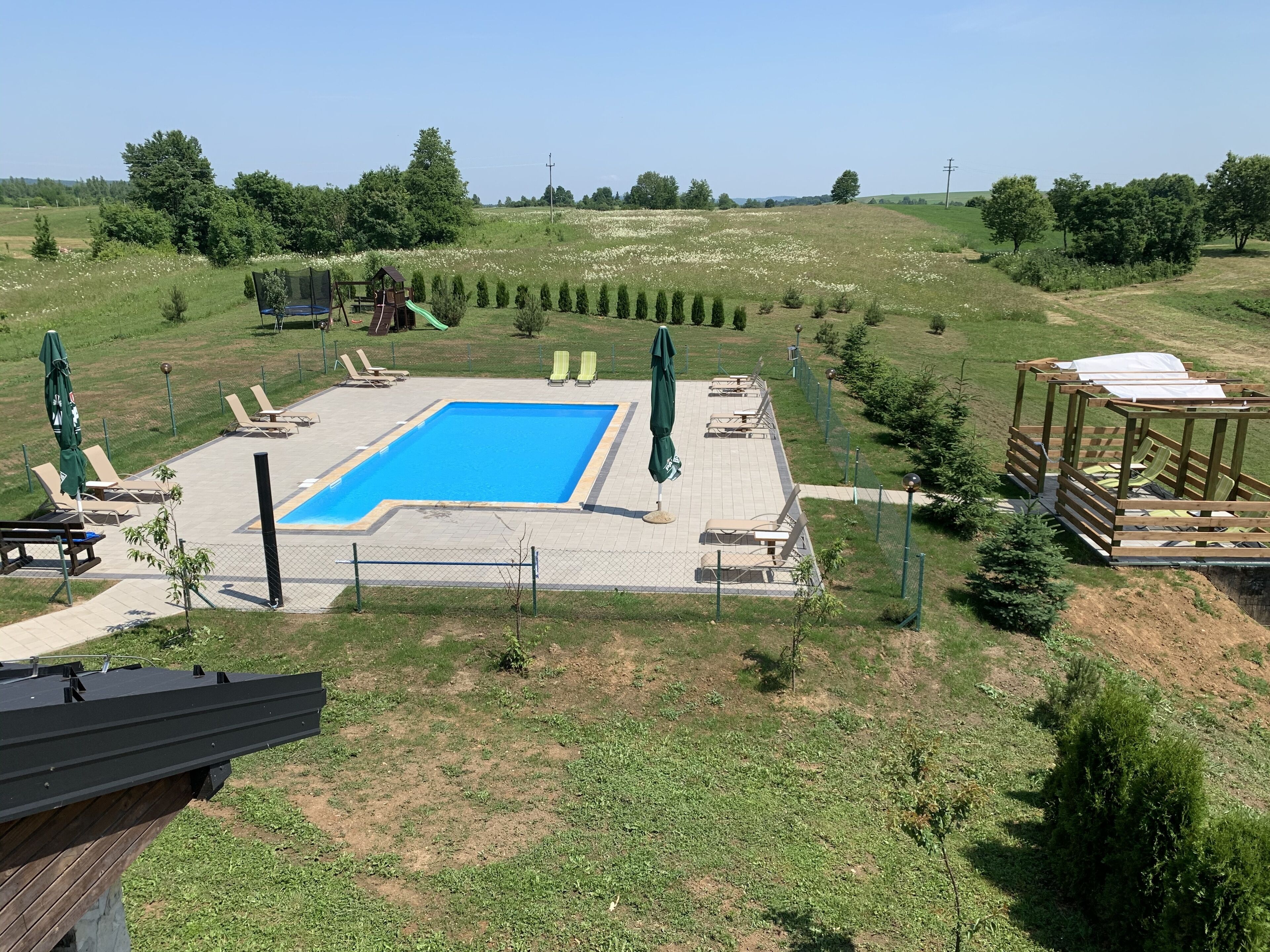 Una piscina rodeada de sillas de descanso y sombrillas, con un muelle de madera y un área cercada.